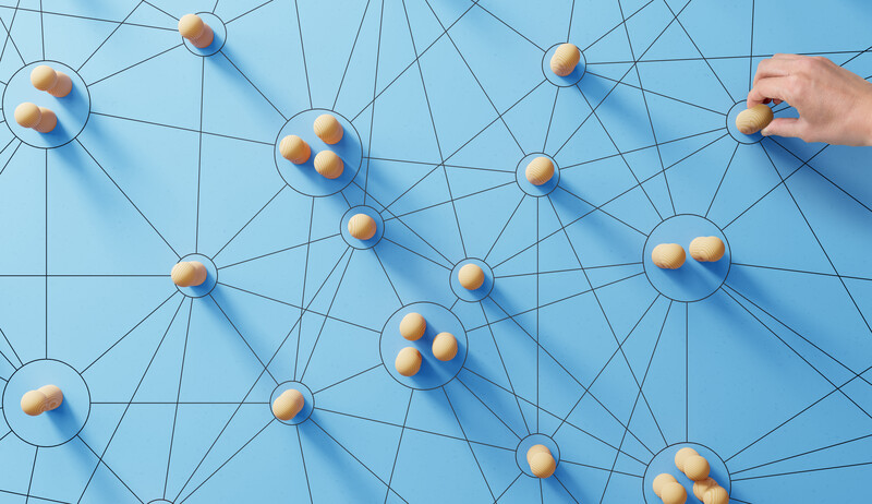 Network diagram with golden spheres connected by blue lines on a light blue background, with a hand reaching toward one node.
