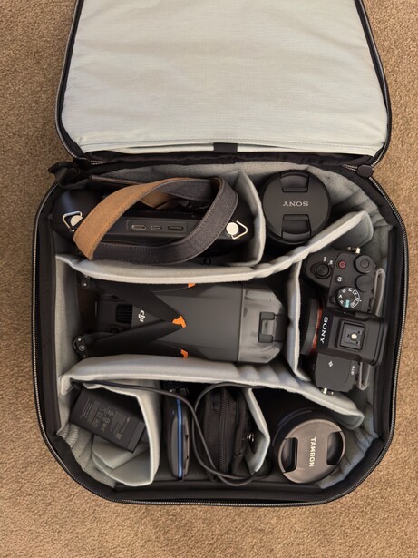 Open camera gear case with organized compartments holding VR headset, controllers, cameras, lenses, batteries, and accessories.