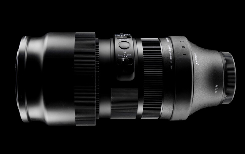Telephoto zoom lens with metal barrel and focus ring against black background.