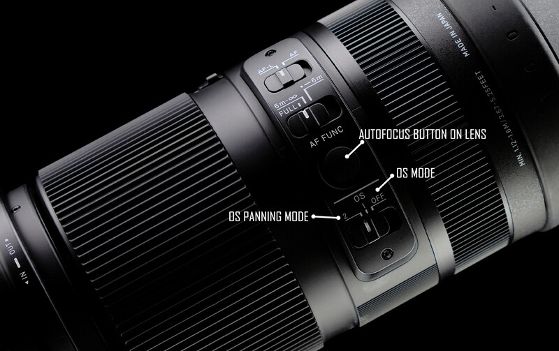 Close-up of a camera lens barrel showing autofocus button, OS mode switch, and OS panning mode controls against black background.
