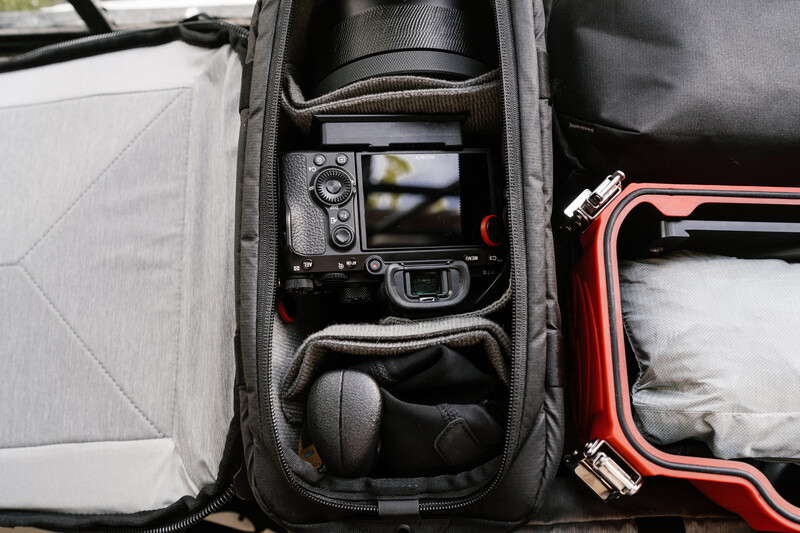 Open camera bag displaying organized compartments with a DSLR camera, lens, and accessories inside.