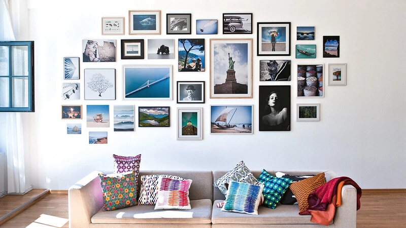 Gallery wall of framed photographs above a gray sofa with colorful patterned pillows and a red blanket.