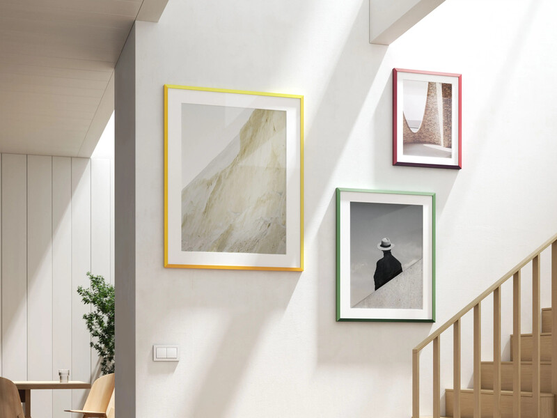 Stairwell with white walls displaying three framed artworks in colored borders against natural light from skylight.