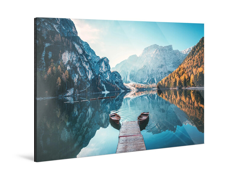Wooden dock extending into a mirror-still alpine lake with two boats, surrounded by steep rocky mountains and golden larch forests.