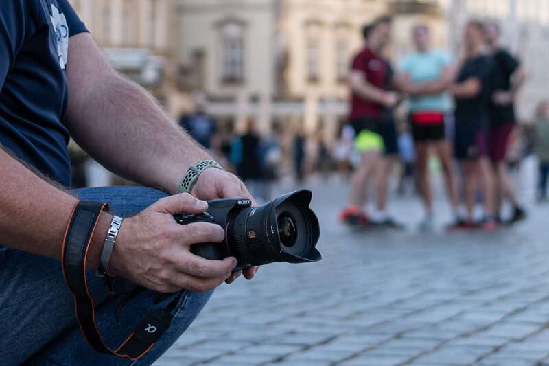 Photographer holding a DSLR camera with telephoto lens in an urban plaza setting.