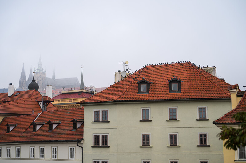 European cityscape with terracotta-roofed buildings and distant cathedral spires under overcast sky.