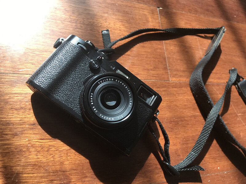 Black rangefinder camera with textured grip and attached fabric neck strap on wooden surface.