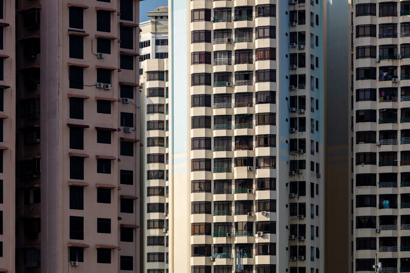 Vertical cityscape of tightly packed residential high-rise buildings with repetitive window patterns and muted earth-tone facades.
