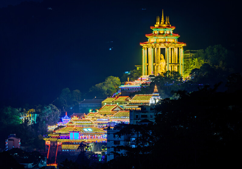 Golden illuminated temple with multiple tiers and spires set against a dark night sky on a hillside.