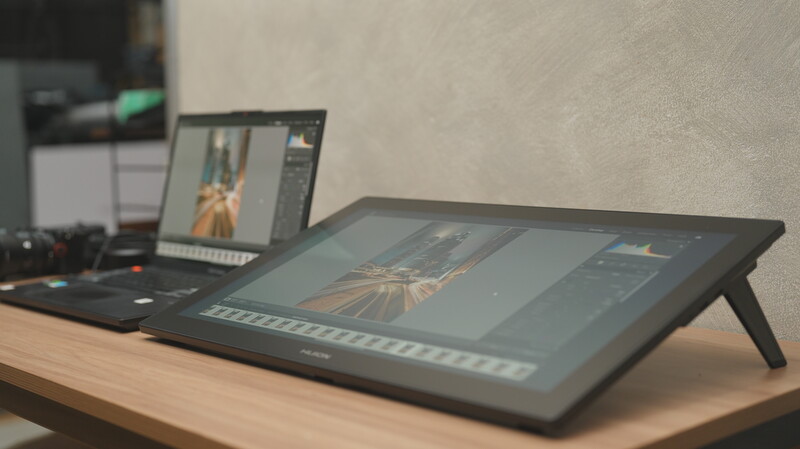 Photographer's desk setup with tablet displaying image editing software and laptop monitor in background.