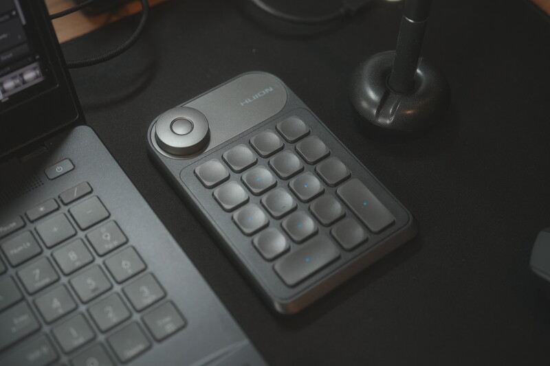 Compact numeric keypad with rotary dial control positioned on dark desk surface next to keyboard.