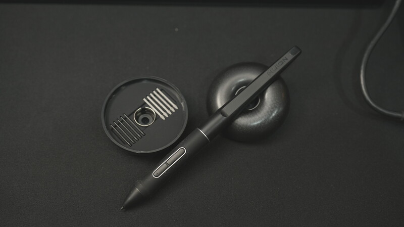 Overhead flat lay of a stylus pen and circular charging pad on a dark surface with cable visible.