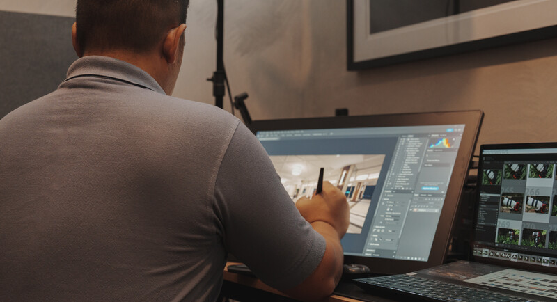 Photographer editing images on a desktop setup with dual monitors displaying post-processing software.