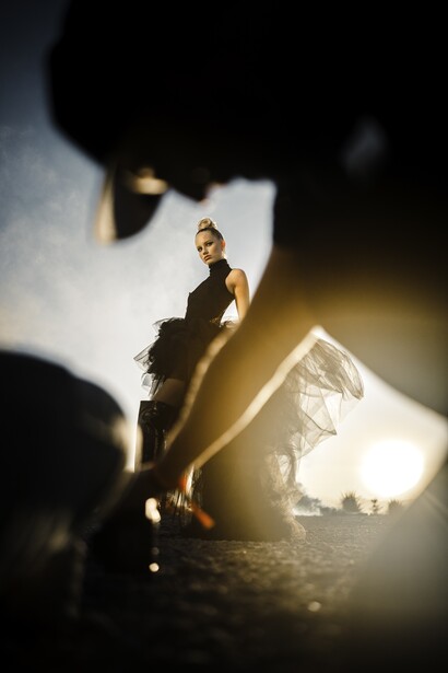 Woman in black clothing stands on a wooden beam, silhouetted against bright backlit fabric.