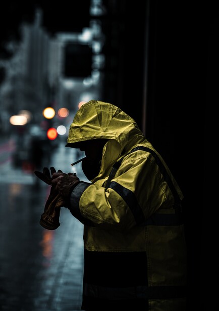 Person in yellow rain jacket holding camera at night on wet street with blurred city lights behind.