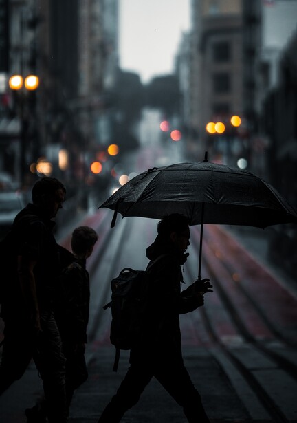 Silhouetted figure holding an umbrella crossing a wet urban street in rain.