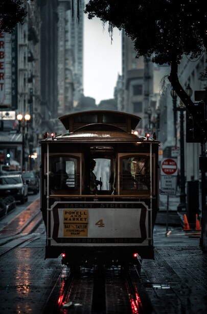 Historic cable car on wet San Francisco street at dusk with illuminated buildings behind.