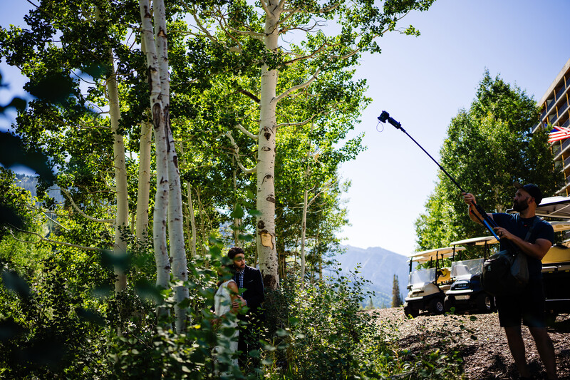 Film crew operating camera and lighting equipment among tall aspen trees in mountainous terrain.