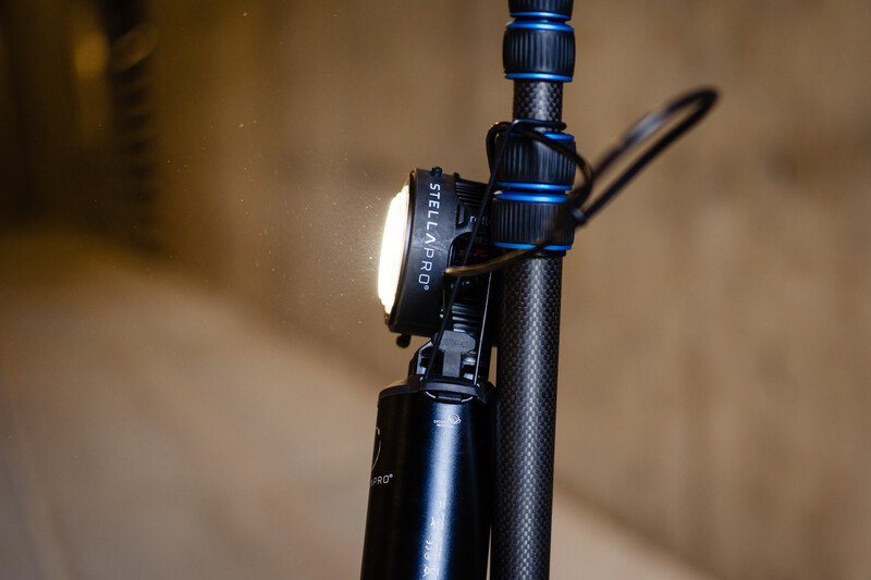 Professional studio light head mounted on a black carbon fiber stand with blue adjustment knobs and control cables.