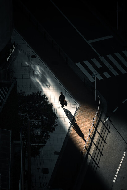 Silhouetted figure descending a staircase in dramatic overhead lighting at night.