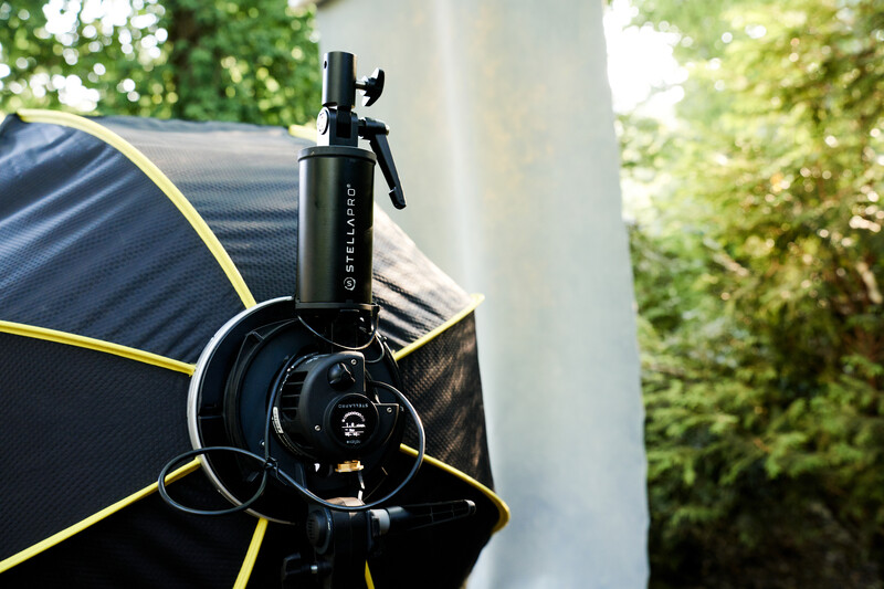 Black studio microphone mounted on boom arm with pop filter and shock mount in outdoor setting.