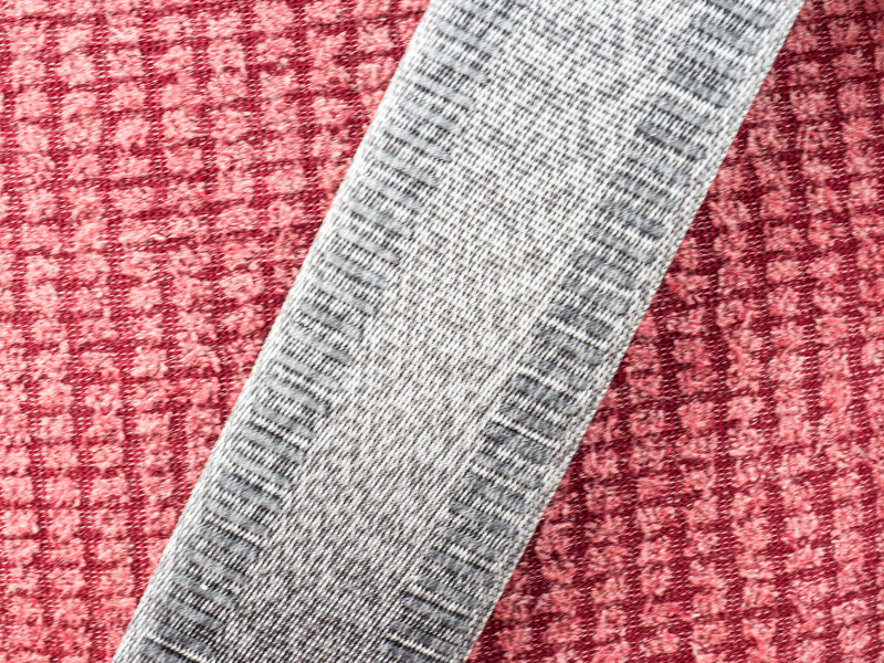 Gray fabric swatch placed diagonally on red textured material.