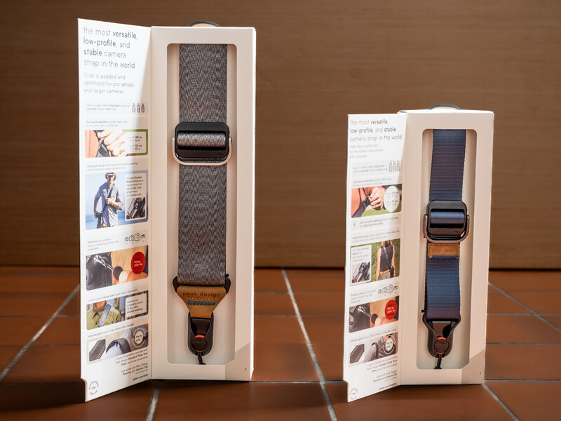 Two camera straps displayed in retail packaging against a brown background, showing different sizes and color options.