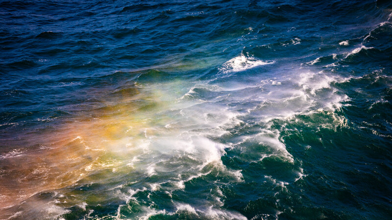 Aerial view of waves breaking on shore with golden and turquoise water creating layered patterns.