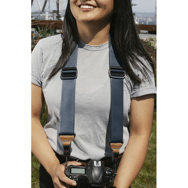 Woman wearing a camera harness system with a DSLR camera in outdoor daylight setting.