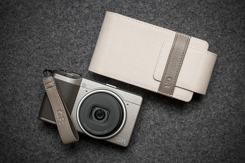Compact camera with attached lens cap and cream-colored protective case on gray felt surface.