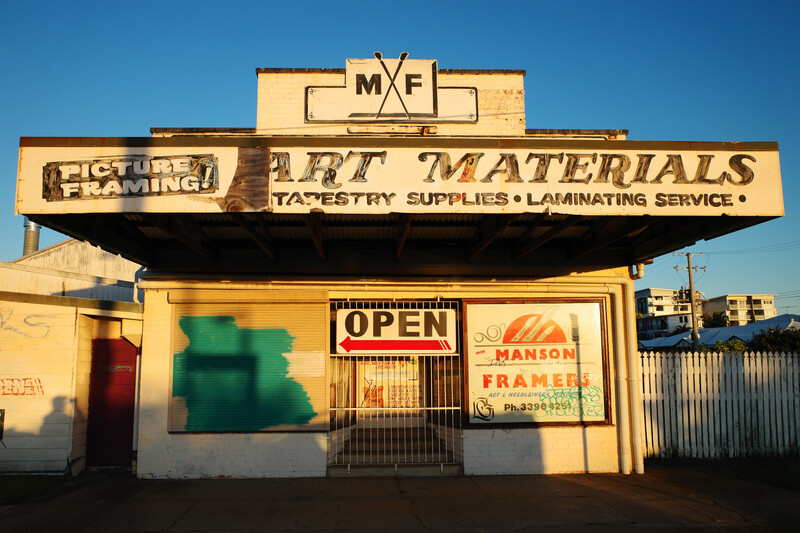 Vintage marquee sign for an art materials store with faded lettering and neon signage against a clear blue sky.