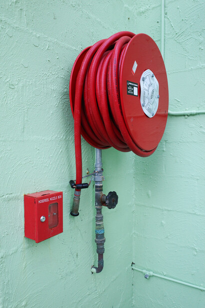 Red fire hose reel mounted on a mint green wall next to a red emergency call box.
