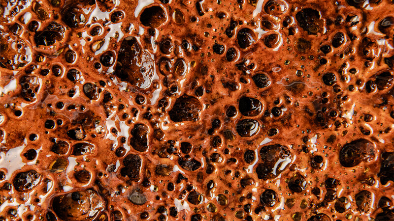 Close-up macro photograph of rust and oxidation texture with irregular holes and metallic surface.