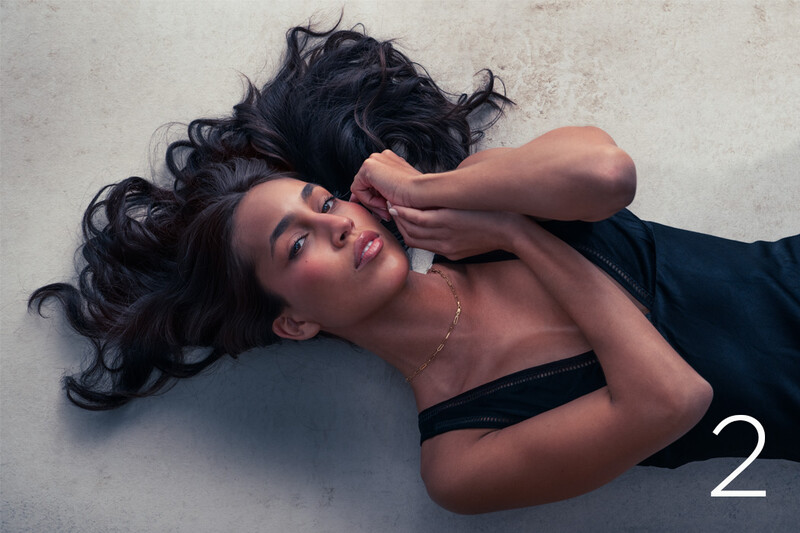 Woman lying on concrete floor with dark wavy hair and neutral expression.