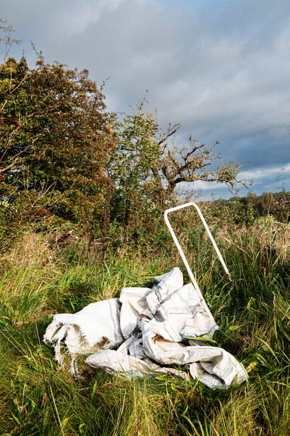 Abandoned white chair lying on its side in overgrown grass beneath cloudy sky.