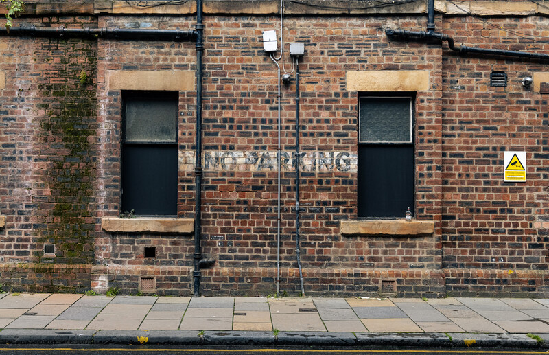 Symmetrical brick facade with two dark rectangular windows and faded signage.