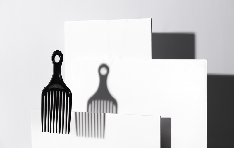 Still life arrangement of two paddle brushes casting shadows against geometric white and dark shapes.