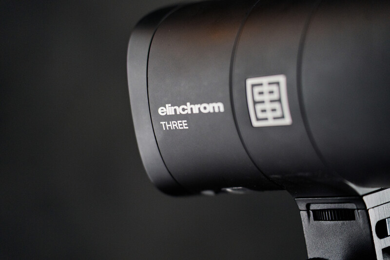 Close-up of an Elinchrom Three monolight head showing the brand name and model designation on its cylindrical body.