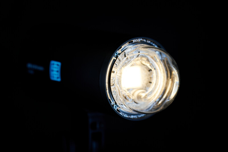 Close-up of a glowing incandescent light bulb against a dark background with blurred blue light source.