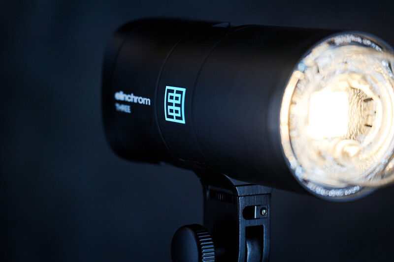 Elinchrom studio flash head illuminated against dark background, showing bright modeling light and control panel.