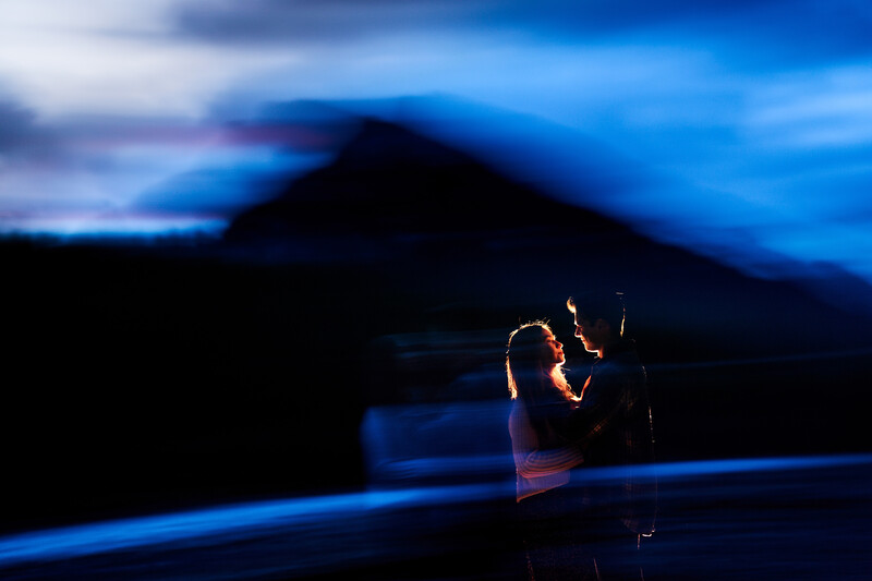 Silhouetted figure holding a phone with a glowing blue light against a dark mountain landscape at dusk.