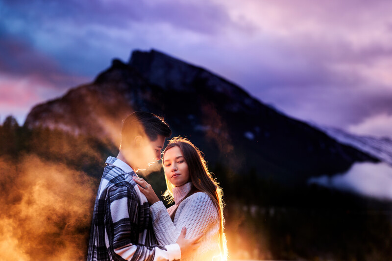 Couple posing together with a mountain silhouette and golden light in the background during dusk.