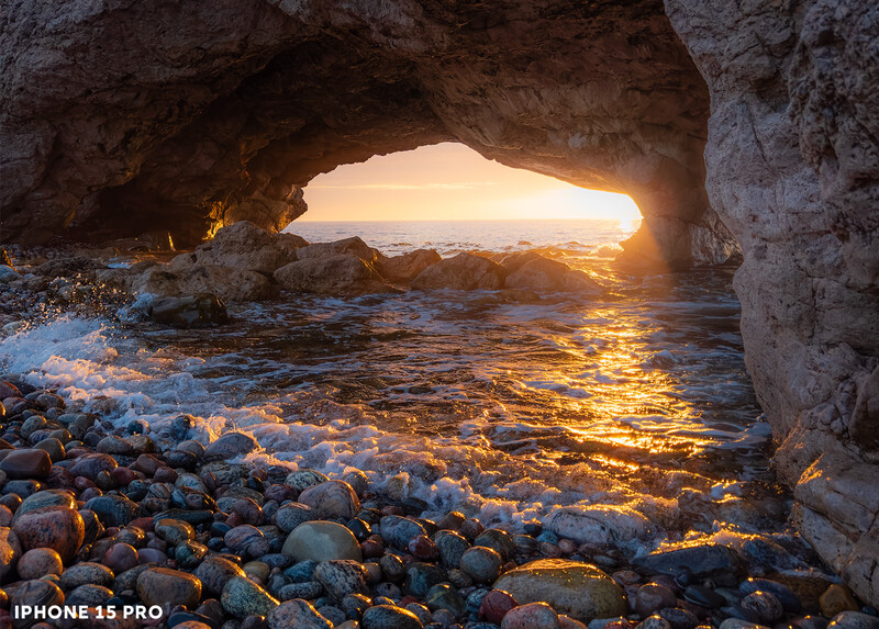 Golden sunset framed through a natural rock cave opening onto a rocky beach and sea.