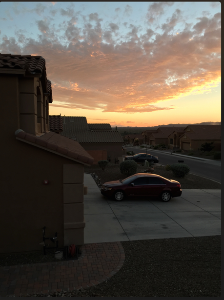 Dramatic sunset sky with golden and orange clouds above a parking lot with parked cars and residential buildings.