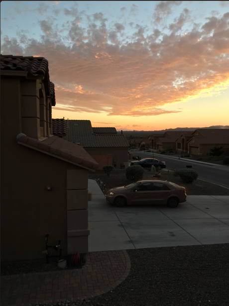 Dramatic sunset sky with golden and orange hues illuminating clouds above a parking lot with parked vehicles.
