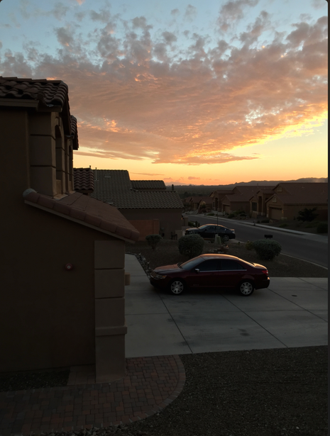 Golden sunset sky with dramatic cloud formations above a parking lot with parked cars and building structures.
