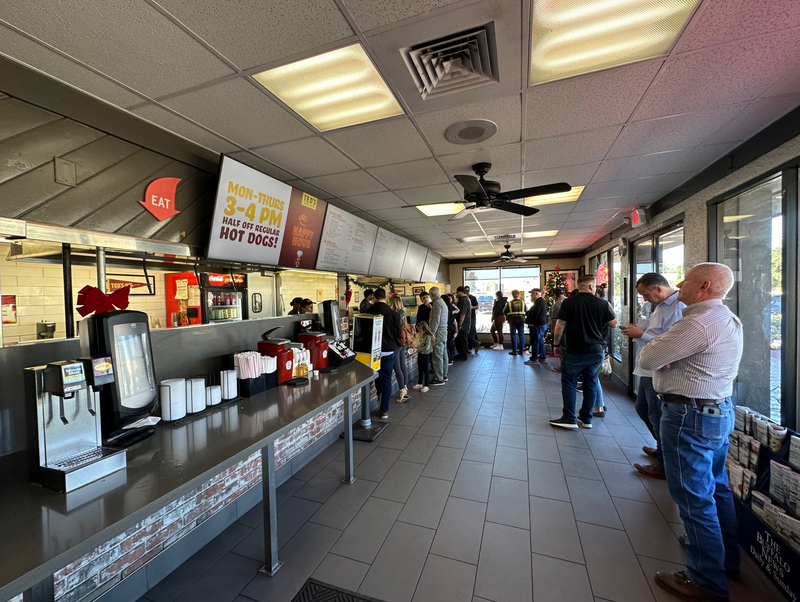 Interior of a fast-casual restaurant with a line of customers waiting at the counter during daytime.