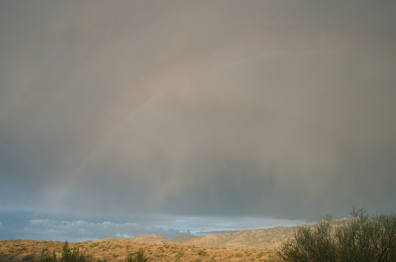 Desert landscape with golden hills under stormy sky with dramatic cloud formation.