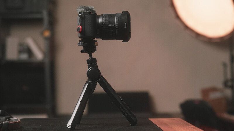 Black mirrorless camera mounted on compact tripod in studio setting with warm lighting.