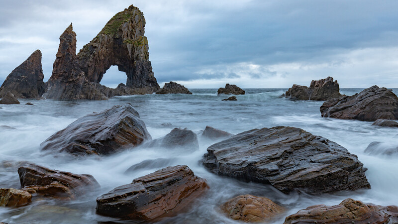 Dramatic rocky coastline with a natural rock arch and smooth water created by long exposure photography.